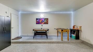 A room with a foosball table, a pool table, and LED strip lighting along the walls.