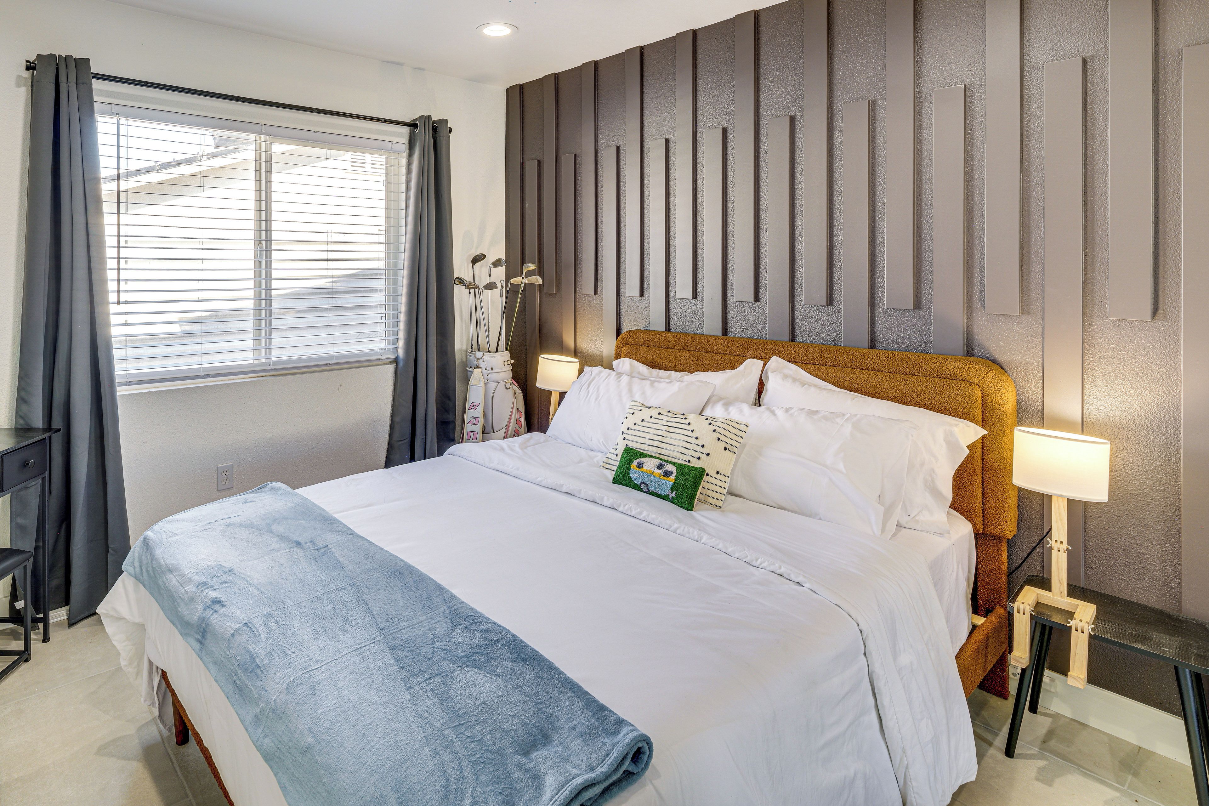 A hotel room with a bed, bedside lamps, a window with curtains, and a wall with vertical panels.