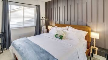 A hotel room with a bed, bedside lamps, a window with curtains, and a wall with vertical panels.