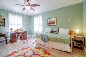 Un dormitorio con cama, mesita de noche, una silla, cómoda, ventilador de techo y una alfombra colorida.
