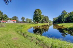 A serene landscape with a pond, grassy areas, and a building with a red roof.