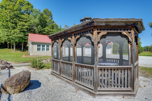 A wooden gazebo with a covered seating area, surrounded by gravel and a large rock.