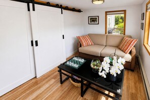 A living room with a sofa, a coffee table with chess pieces and a plant, and a sliding door. - Ketchikan Oceanfront Retreat | Dock On-Site, Beach (Ketchikan)
