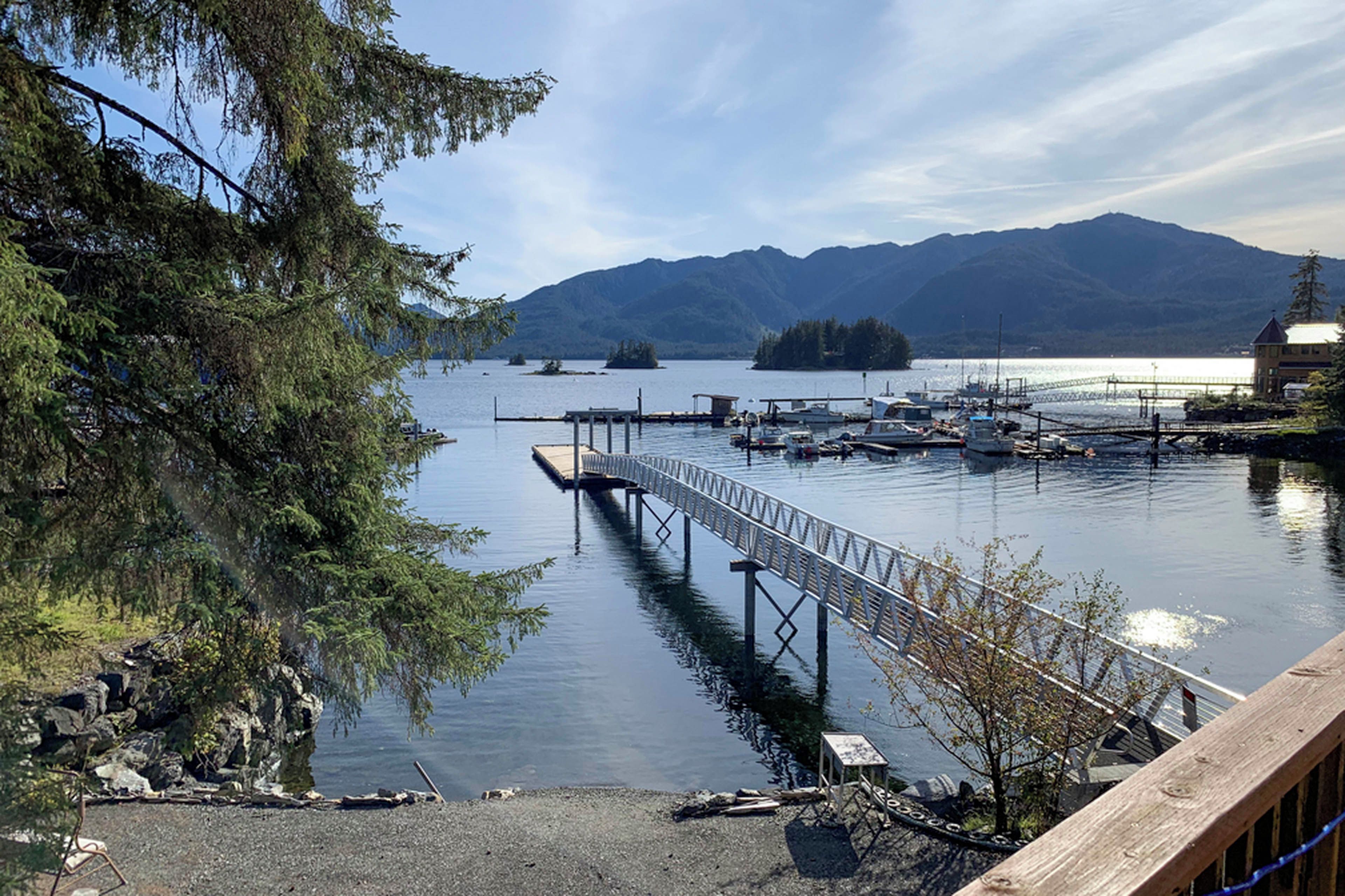 A calm lake with a dock extending into the water, surrounded by trees and mountains in the background.