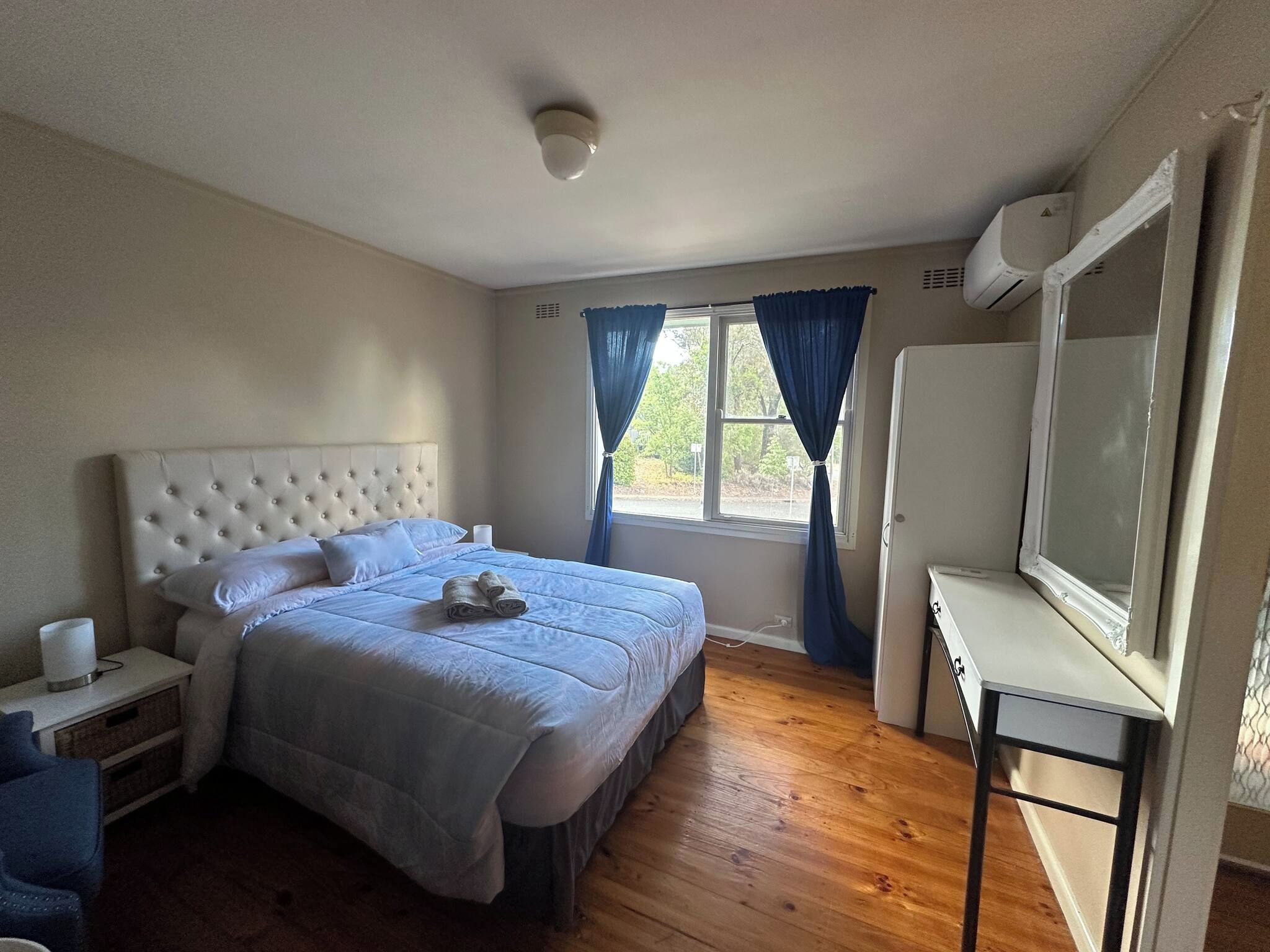 A bedroom with a bed, a bedside table, a TV, and a window with curtains.