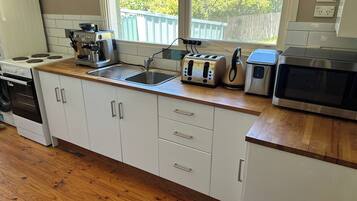 A kitchen with white cabinets, a wooden countertop, a sink, a stove, a toaster, and a microwave.