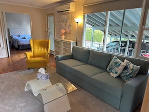 A living room with a sofa, a yellow armchair, a glass coffee table, and a bed in the background. - Locum Welcome Home - Close to Canberra Hospital (Garran)