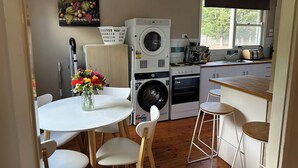 Cocina compacta con lavadora, cafetera y comedor con mesa y sillas.