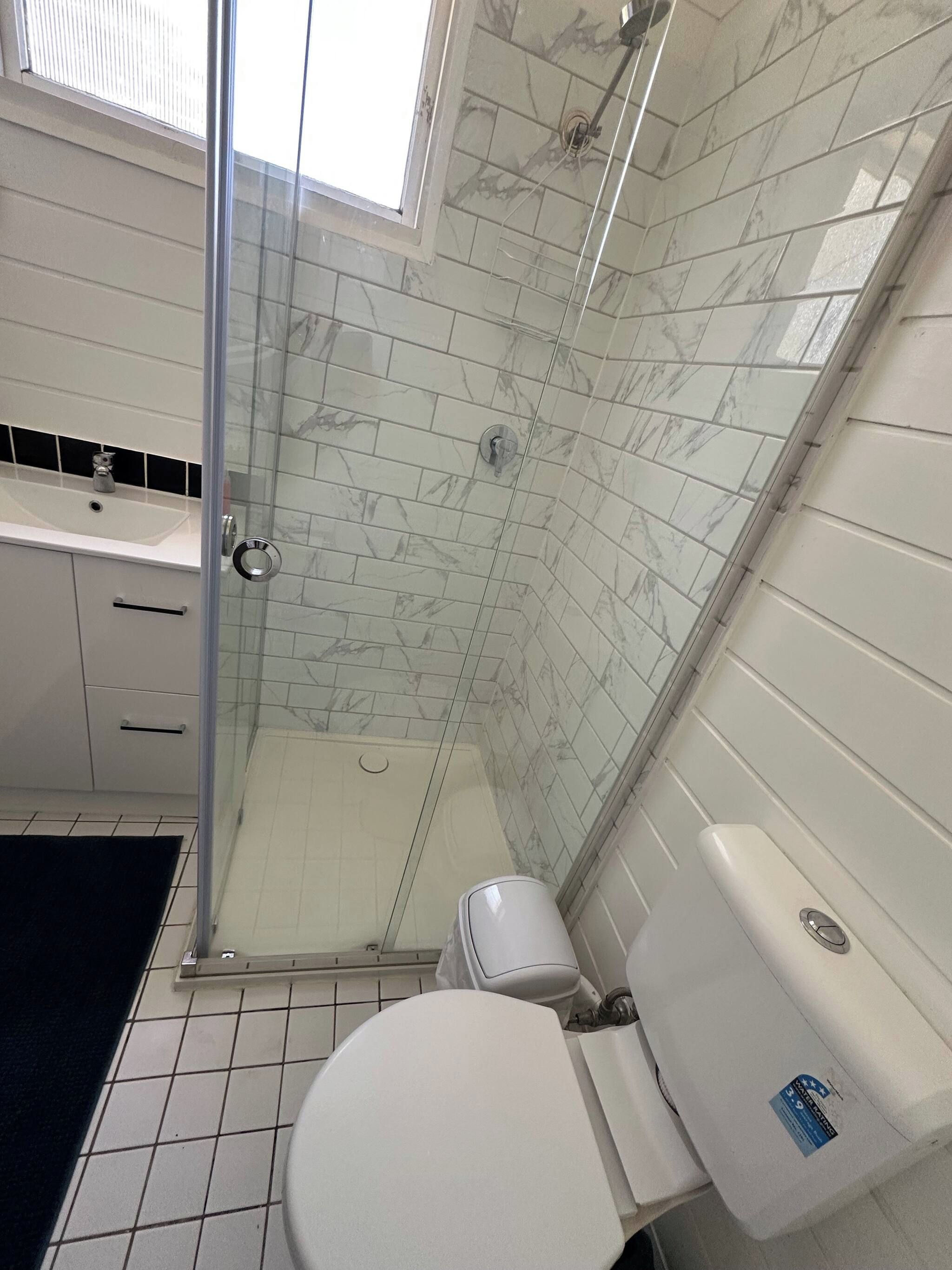 A bathroom with a glass-enclosed shower, white toilet, and a sink with a black countertop.