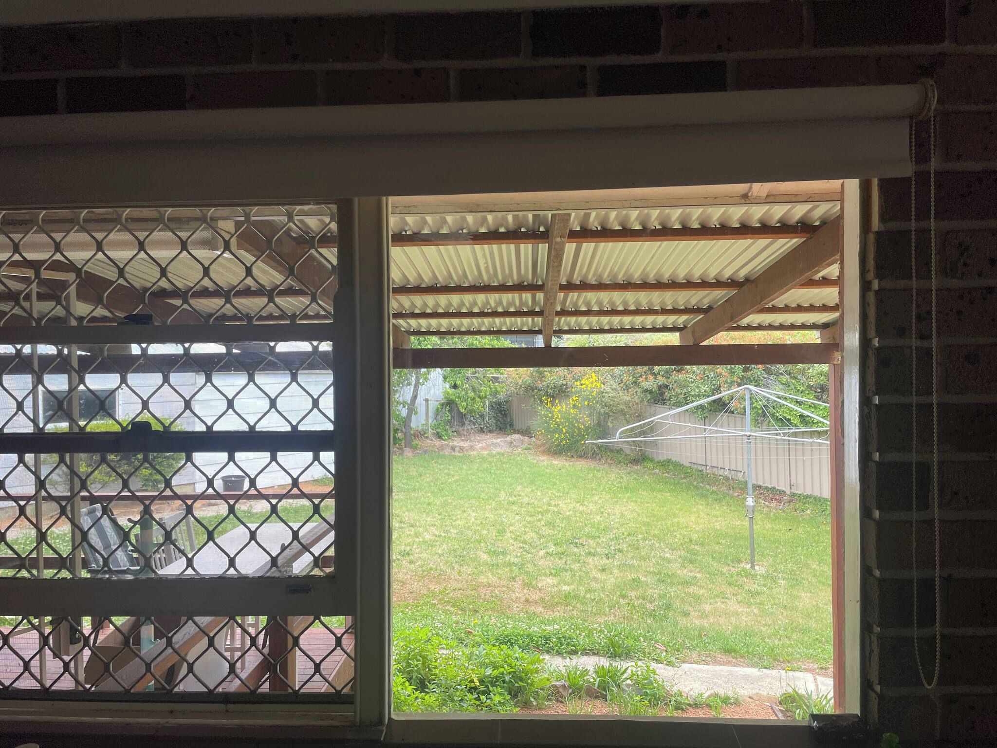 A view through a window with a metal grid, a covered outdoor area, and a grassy yard.