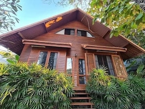 A two-story wooden house with a steeply pitched roof, multiple windows, and a staircase leading to the entrance.