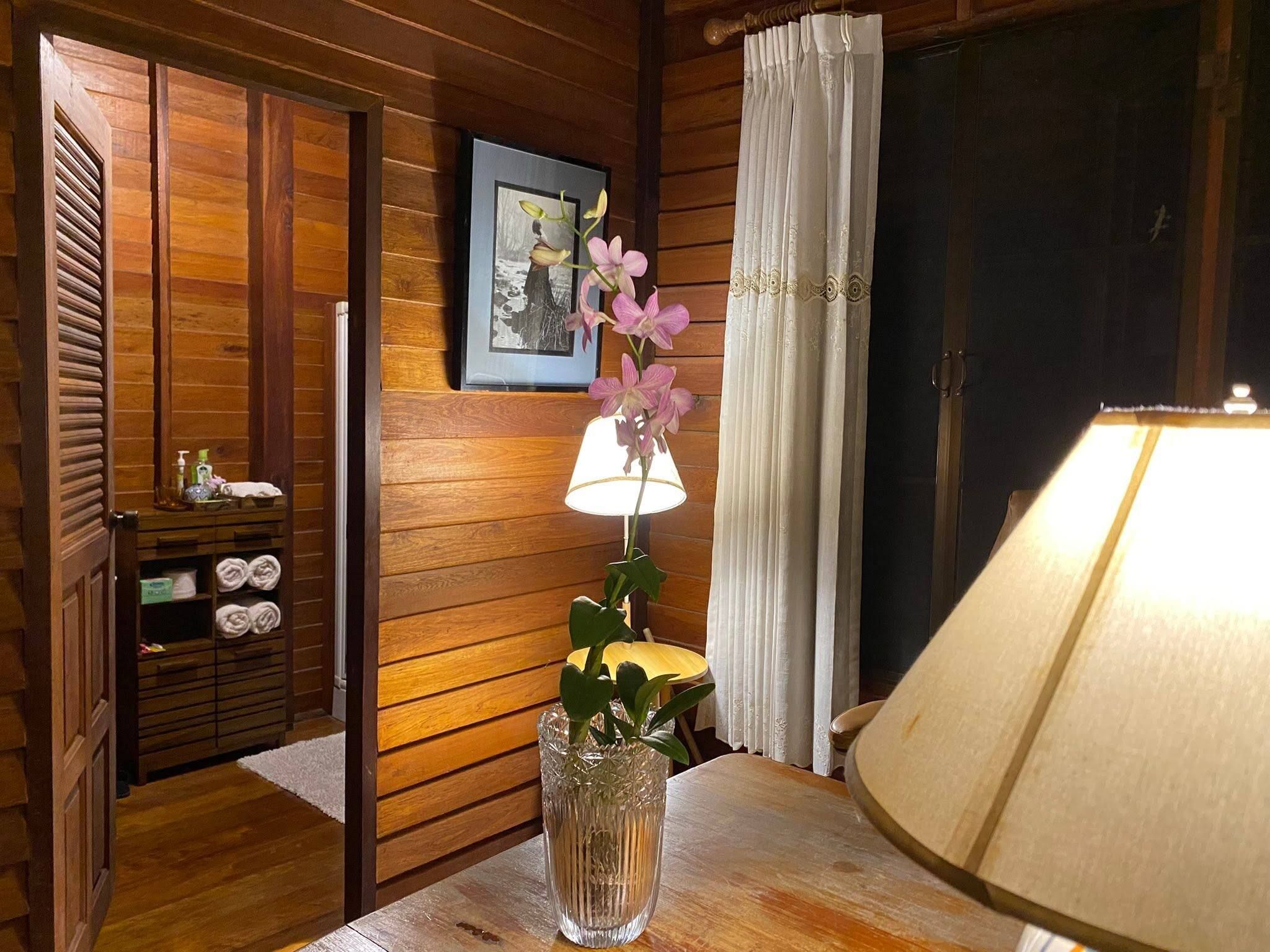 A wooden interior with a lamp, a vase with flowers, and a framed picture on the wall.