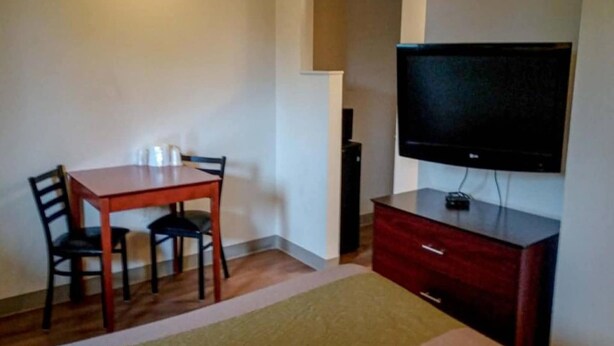 Een hotelkamer met een houten tafel, twee stoelen, een televisie op een dressoir en een rode kast.