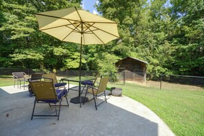 An outdoor patio with a table and chairs, a large umbrella, and a wooden shed in a wooded area. - Wine Country Retreat! Sun Porch, Private Yard (Lexington)