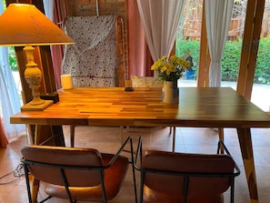 A dining area with a wooden table, two chairs, a lamp, and a vase with flowers. - the NOW by Kru Se Cottage (Chiang Mai)