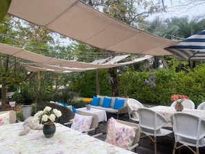 An outdoor patio area with tables and chairs, covered by a canopy, surrounded by greenery. - the NOW by Kru Se Cottage (Chiang Mai)
