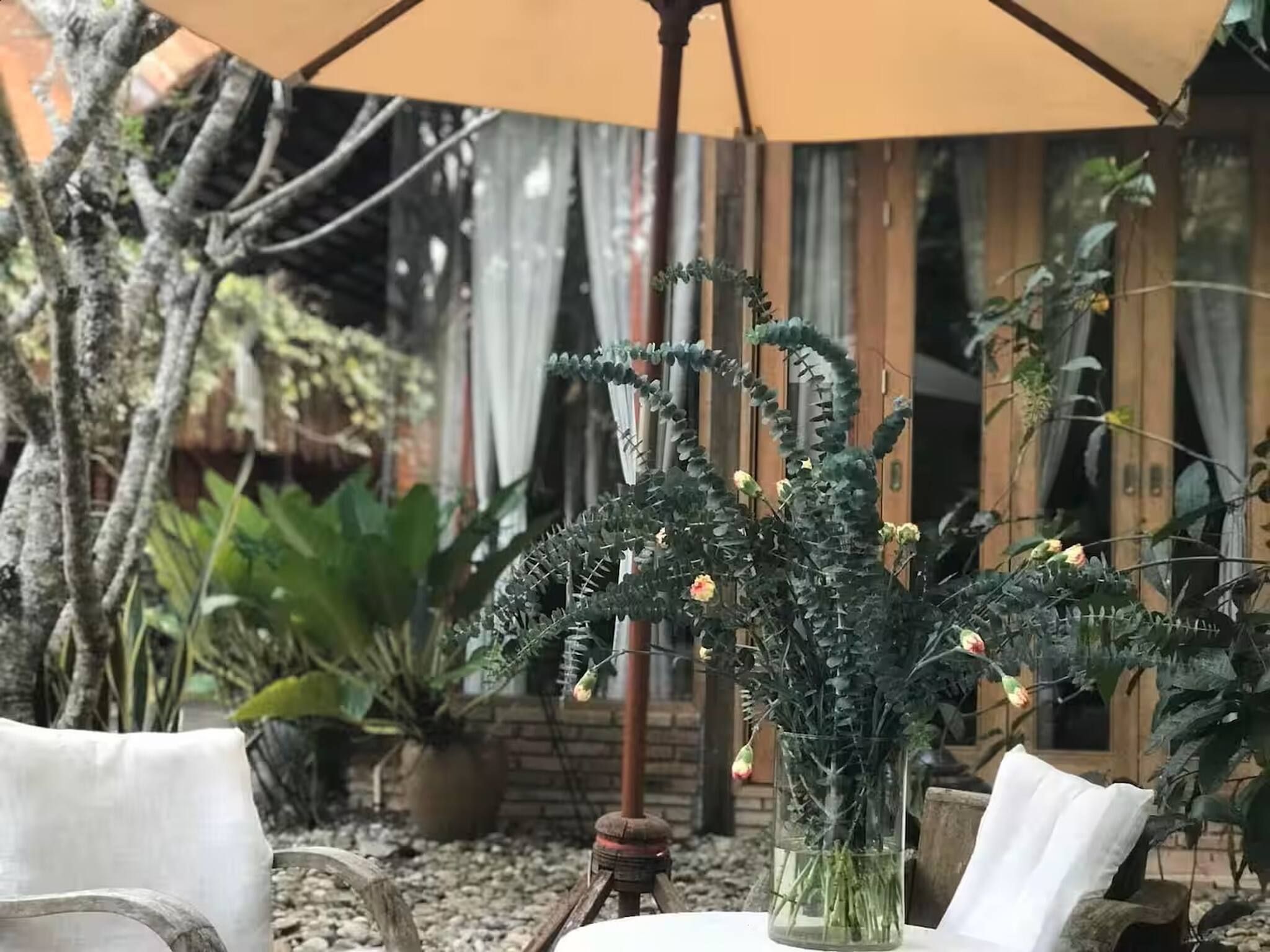 A table with a glass vase of plants, outdoor seating, and a wooden chair.