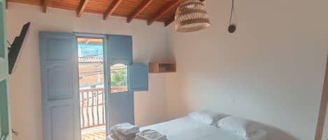 A bedroom with a wooden ceiling, a bed with white linens, a hanging light fixture, and a view through an open door.