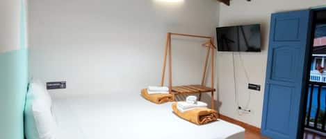 Una habitación con cama, un banco de madera, una lámpara colgante, un televisor montado en la pared y una puerta azul.