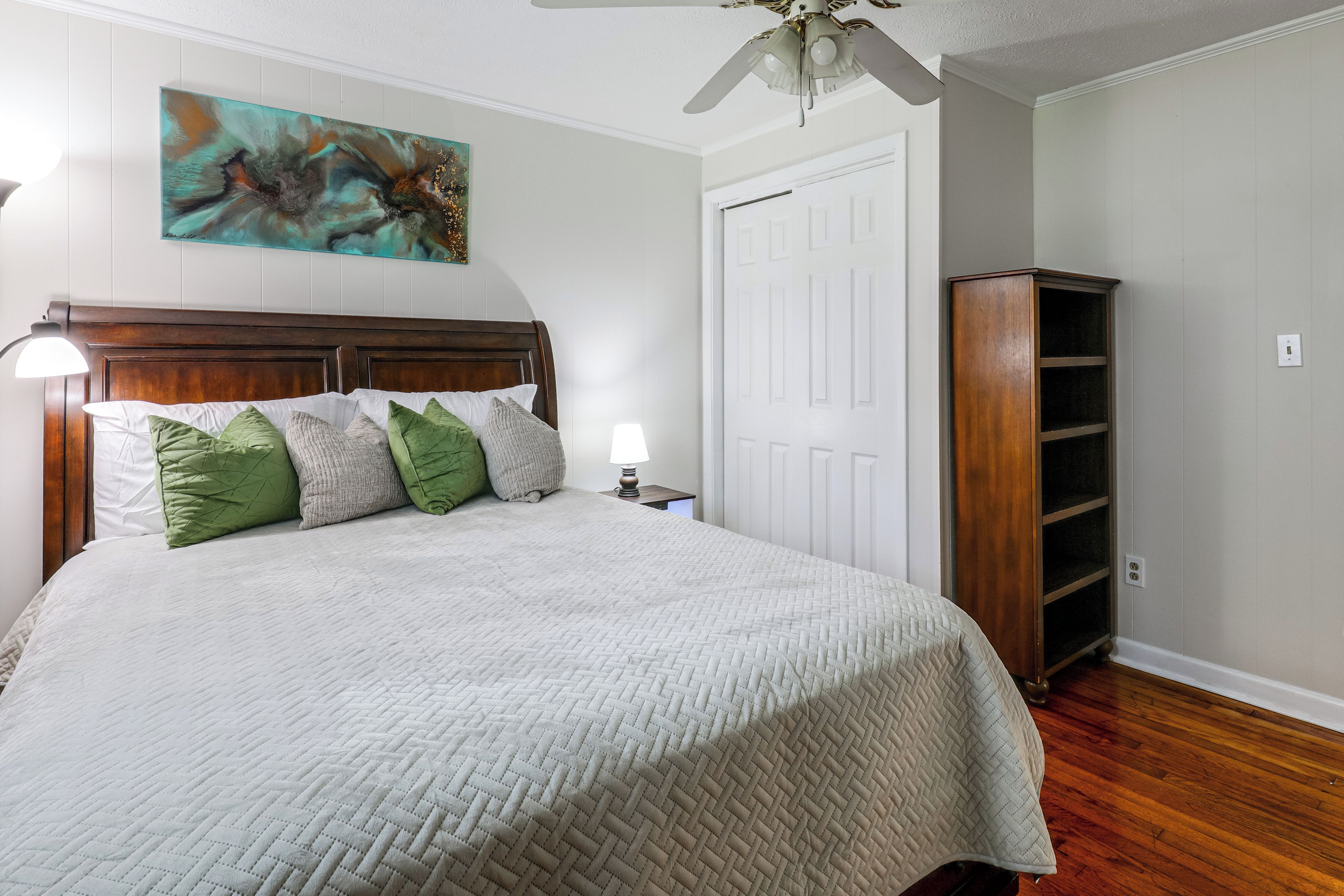 A bedroom with a bed, pillows, a nightstand, a wall art piece, a door, and a built-in bookshelf.