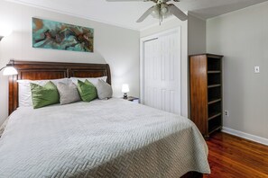 Un dormitorio con cama, almohadas, una mesita de noche, una obra de arte en la pared, una puerta y una estantería empotrada.