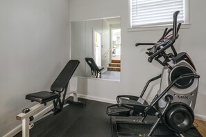 Ein Fitnessraum mit einer Bank, Laufband und einer Spiegelwand, die eine Treppe und eine Küche reflektiert.