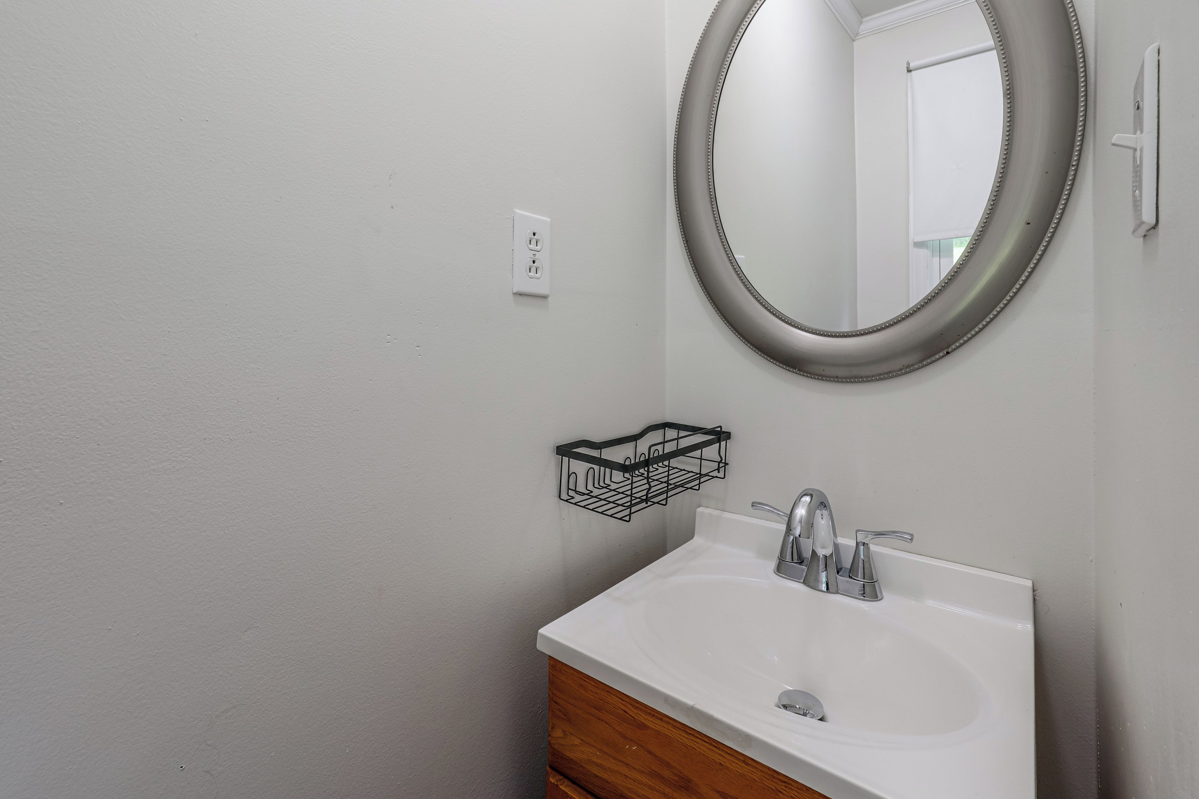 A bathroom with a white sink, a mirror, and a black wall-mounted basket.