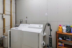 Une buanderie équipée d’un lave-linge et d’un sèche-linge à chargement frontal, d’une étagère contenant des produits de nettoyage et d’un chauffe-eau.