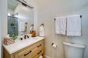 Ein Badezimmer mit einem weißen Waschbecken, einem Holzauszug, einem Spiegel, zwei an der Wand hängenden Handtüchern und einer Toilette.