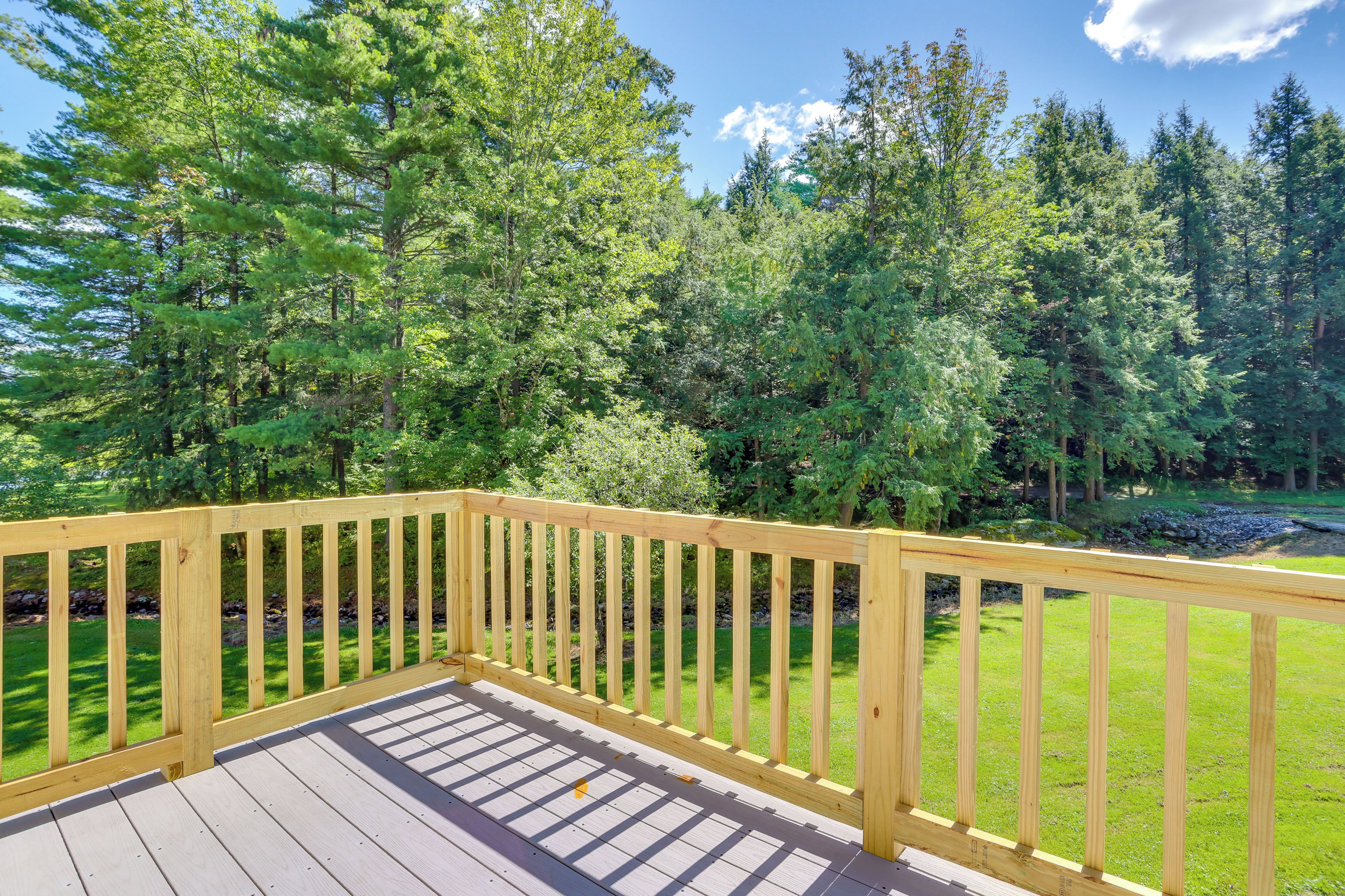 A wooden deck with a railing, surrounded by a grassy area and dense trees.