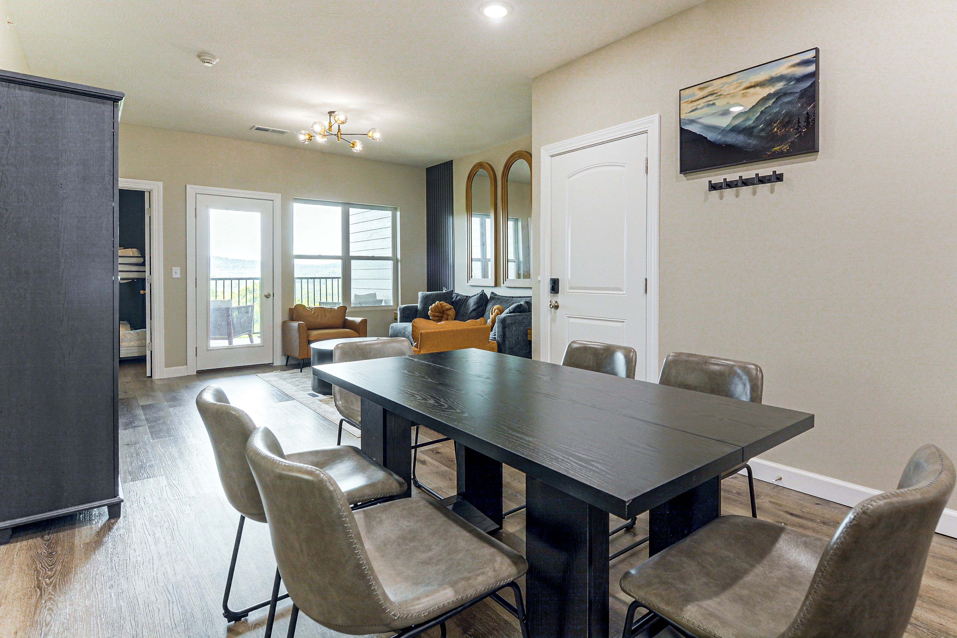 A dining area with a dark wooden table and cushioned chairs, a white door, and a large window with a view.