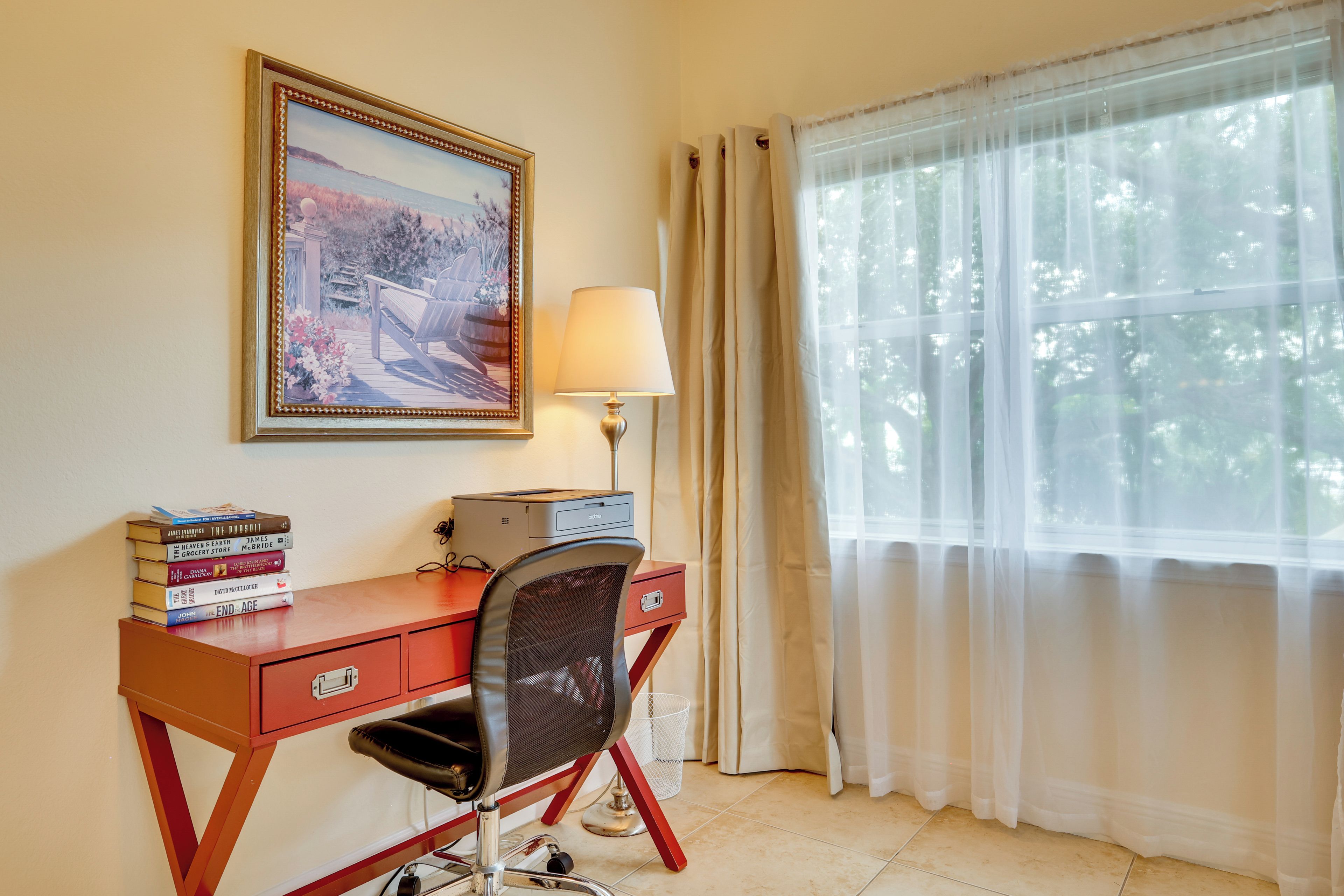 Una habitación con escritorio, silla, lámpara y ventana con cortinas.