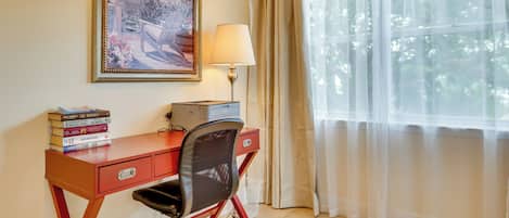 Una habitación con escritorio, silla, lámpara y ventana con cortinas.