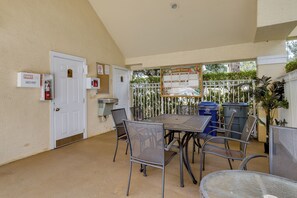 A covered outdoor patio with a table and chairs, a first aid sign, a fire extinguisher, and a recycling bin. - Venetian Palms Condo: Pool, Hot Tub & Tennis! (Fort Myers)