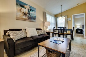 A living room with a dark brown sofa, a wooden coffee table, and a painting of a horse. - Venetian Palms Condo: Pool, Hot Tub & Tennis! (Fort Myers)