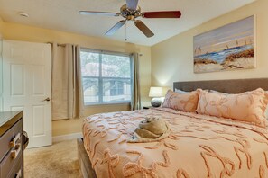 A bedroom with a bed, a ceiling fan, a window with curtains, a nightstand with a lamp, and a painting on the wall. - Venetian Palms Condo: Pool, Hot Tub & Tennis! (Fort Myers)