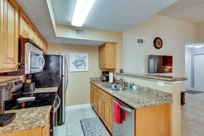 A kitchen with wooden cabinets, a stainless steel refrigerator, a microwave, a stove, and a granite countertop. - Venetian Palms Condo: Pool, Hot Tub & Tennis! (Fort Myers)