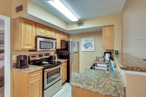 A kitchen with wooden cabinets, a stainless steel refrigerator, a microwave, a stove, and granite countertops. - Venetian Palms Condo: Pool, Hot Tub & Tennis! (Fort Myers)