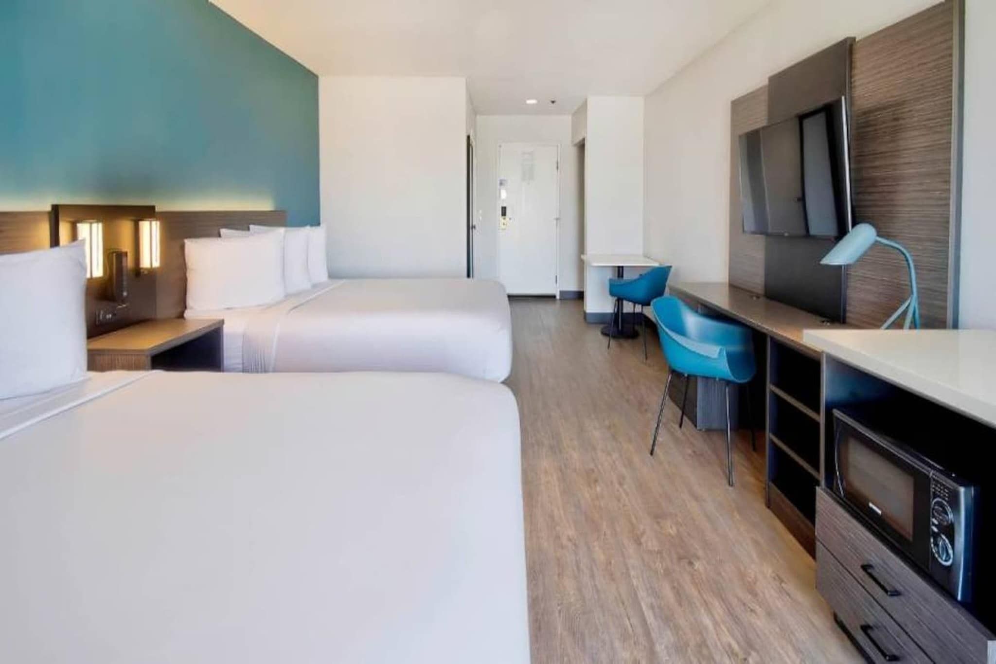 A hotel room with two beds, a desk, a chair, a TV, and a microwave.