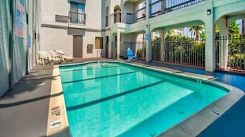 Une piscine à l’eau d’un bleu cristallin, entourée d’un immeuble à plusieurs niveaux doté de balcons et d’une galerie couverte.
