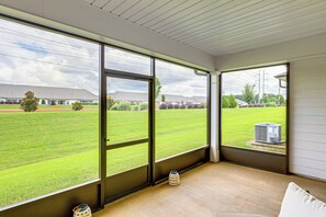 A room with large windows offering a view of a grassy field and a building in the distance. - Screened Porch: Newly Built Townhome in Madison (Madison)