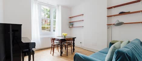 Un salon avec un piano, un canapé bleu, un parquet en bois et une fenêtre donnant sur un paysage verdoyant.