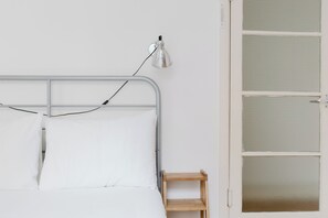 Ein Bett mit Metallgestell, weißer Bettwäsche und einem Nachttisch mit Lampe.