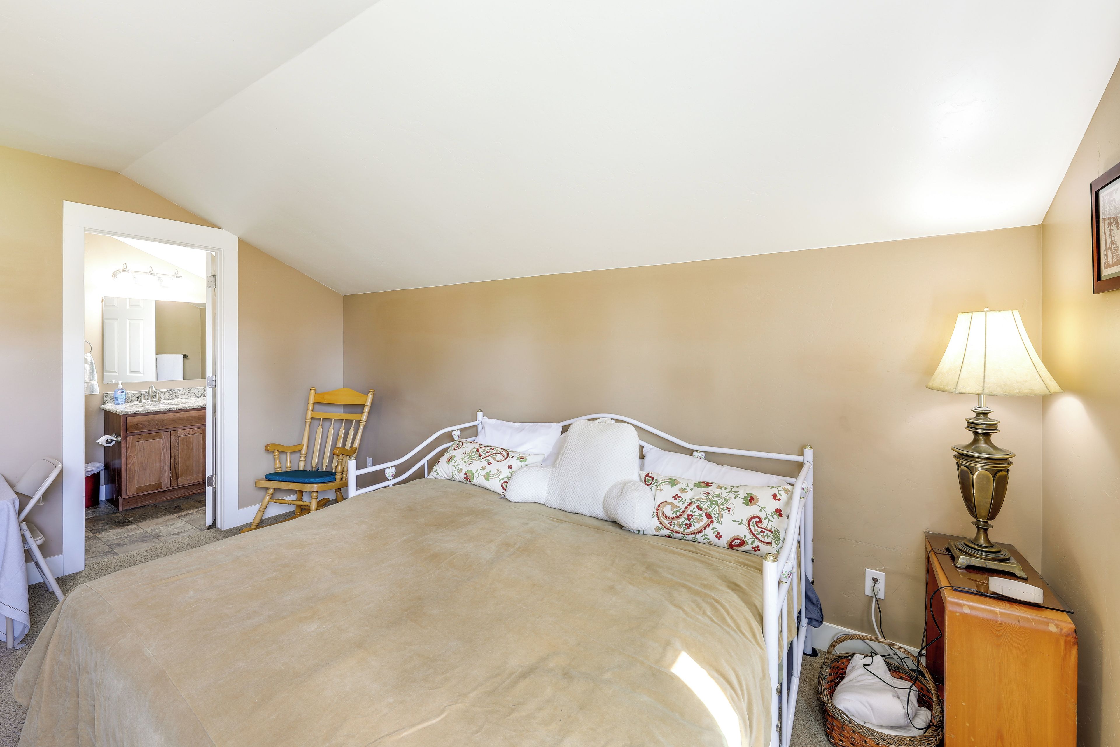 A bedroom with a bed, a chair, a bedside table, a lamp, and a dresser.