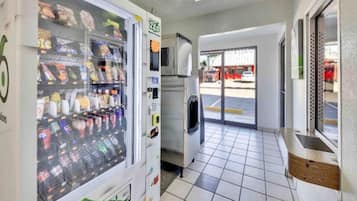 Una máquina expendedora con diferentes aperitivos y bebidas, un refrigerador y un piso de baldosas en un espacio comercial.