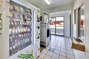 A vending machine with various snacks and drinks, a refrigerator, and a tiled floor in a commercial space.