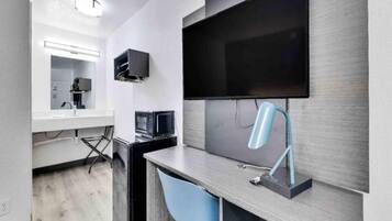 A modern room with a flat-screen TV mounted on the wall, a desk with a chair, and a compact kitchenette area.