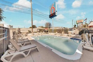 A swimming pool with lounge chairs, a large sign with the number 6, and a fenced area.