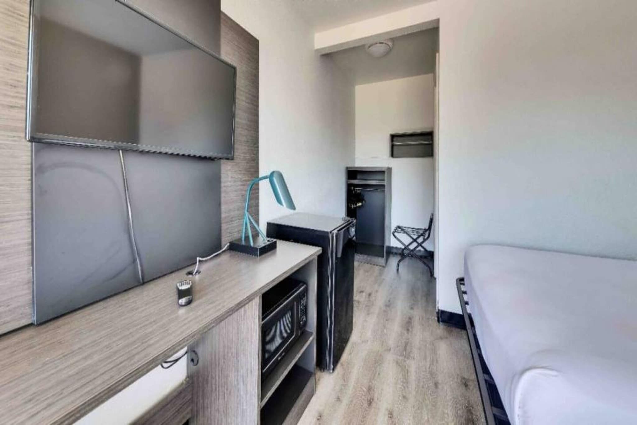 Habitación de hotel moderna con televisión de pantalla plana, escritorio con lámpara, microondas y zona de comedor con una silla.