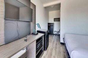 A modern hotel room with a flat-screen TV, a desk with a lamp, a microwave, and a dining area with a chair.